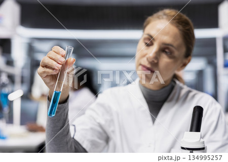 Close up of scientist doing food safety inspection in lab, analyzing blue food coloring additive in test tube sample. Female researcher verifying chemical safety compliance for consumer food products Close up of scientist doing food safety inspection in lab, analyzing blue food coloring additive in test tube sample. Female researcher verifying chemical safety compliance for consumer food products 134995257