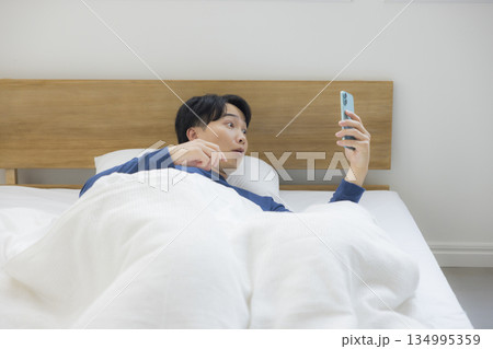 ベッドでスマホを見る若い男性 ベッドでスマホを見る若い男性 134995359