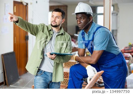 Worker and owner building discuss construction plan inside building under construction Worker and owner building discuss construction plan inside building under construction 134997750