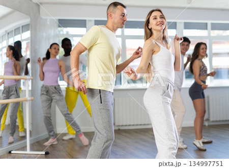 Happy young woman and man with group of multinational people enjoying active boogie-woogie dance in studio 134997751