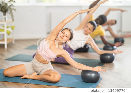 Young woman doing pilates with soft ball in group 134997764