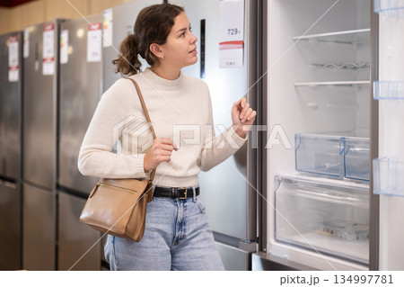 Young woman chooses refrigerator in appliance store Young woman chooses refrigerator in appliance store 134997781