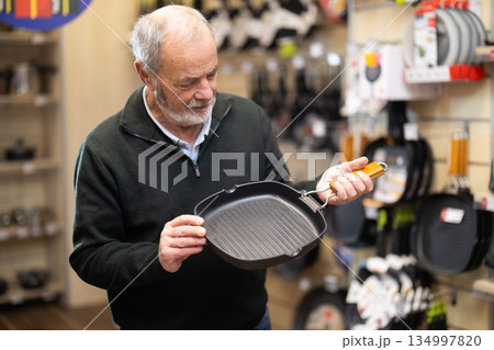 Elderly man chooses teflon-coated frying pan iron at supermarket 134997820