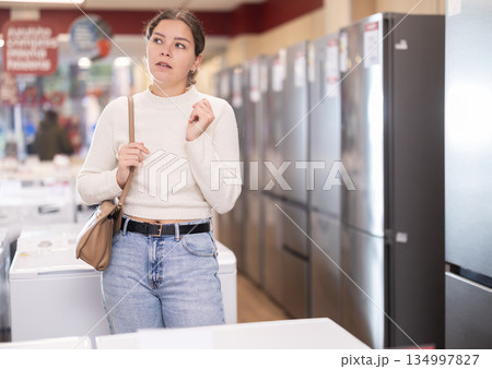 Young woman chooses refrigerator in appliance store Young woman chooses refrigerator in appliance store 134997827