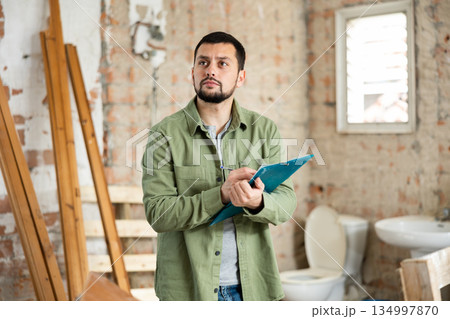 Focused man standing at indoors building site, reading document 134997870