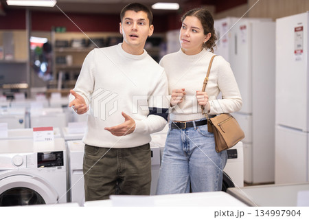 Young couple choosing washing machine or dishwasher Young couple choosing washing machine or dishwasher 134997904