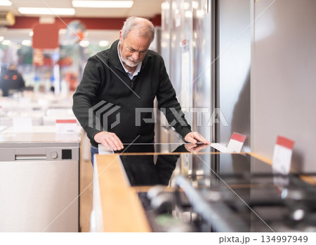 Senior man customer inspect product range and selects kitchen oven Senior man customer inspect product range and selects kitchen oven 134997949