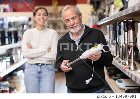 Senior man and gir examines kitchen blender in detail before buying 134997991