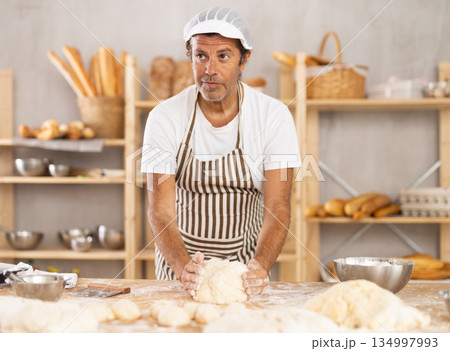 Adult male baker kneading dough on table Adult male baker kneading dough on table 134997993