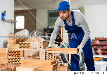 Portrait of a worker in blue overalls with brick panels in hands Portrait of a worker in blue overalls with brick panels in hands 134998131