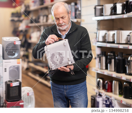 Eldery man chooses portable heater in appliance store Eldery man chooses portable heater in appliance store 134998258
