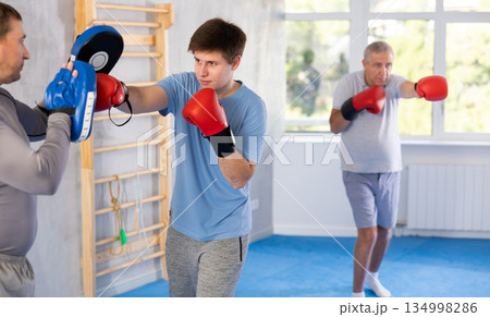 Boxing training - young guy masters boxing strikes on trainer punch mitts during training 134998286