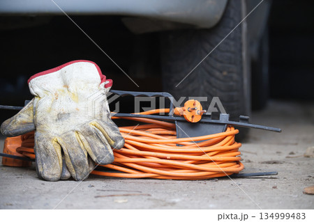 Work gloves and coiled orange extension cord resting on concrete near a car tire 134999483