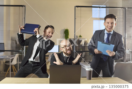 Playful businessmen and coworkers celebrate office success with laptop, clipboard Playful businessmen and coworkers celebrate office success with laptop, clipboard 135000375