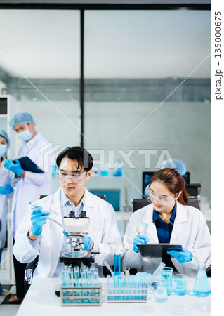 Team of scientists analyzing blue liquid samples in a modern lab, showcasing biotechnology, chemistry, and medical research innovation. Team of scientists analyzing blue liquid samples in a modern lab, showcasing biotechnology, chemistry, and medical research innovation. 135000675