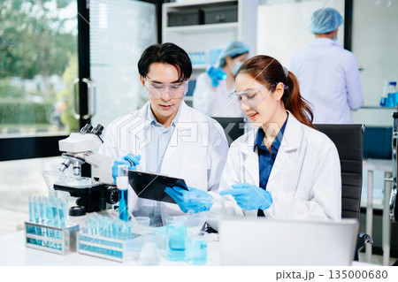Scientists collaborating in a modern lab with microscopes and blue liquids, representing biotechnology, chemistry, and medical research innovation. Scientists collaborating in a modern lab with microscopes and blue liquids, representing biotechnology, chemistry, and medical research innovation. 135000680