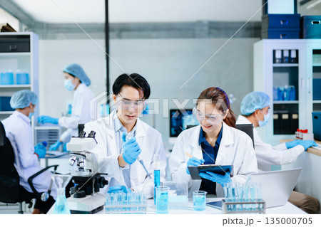 Scientists collaborating in a modern lab with microscopes and blue liquids, representing biotechnology, chemistry, and medical research innovation. 135000705