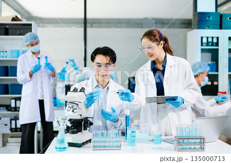 Scientists collaborating in a modern lab with microscopes and blue liquids, representing biotechnology, chemistry, and medical research innovation. 135000713