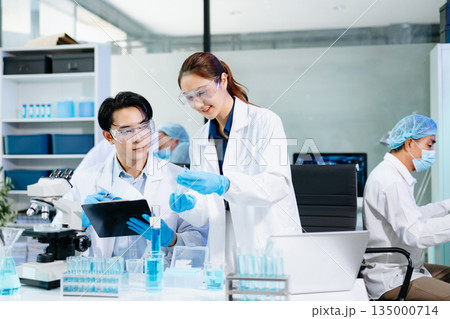 Scientists collaborating in a modern lab with microscopes and blue liquids, representing biotechnology, chemistry, and medical research innovation. 135000714