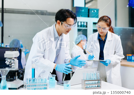 Scientists collaborating in a modern biotechnology lab with microscopes and test tubes, symbolizing teamwork, chemistry, and scientific innovation. 135000740