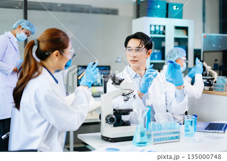 Professional scientists analyzing samples in a modern lab with blue liquids and microscopes, representing biotechnology, chemistry, and healthcare innovation. Professional scientists analyzing samples in a modern lab with blue liquids and microscopes, representing biotechnology, chemistry, and healthcare innovation. 135000748