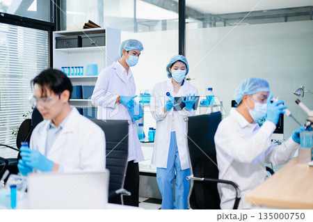 Scientists collaborating in a modern biotechnology lab with microscopes and test tubes, symbolizing teamwork, chemistry, and scientific innovation. 135000750