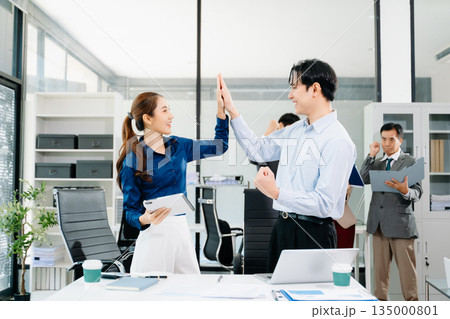 Happy Asian business team celebrating success with a high five in a modern office Happy Asian business team celebrating success with a high five in a modern office 135000801