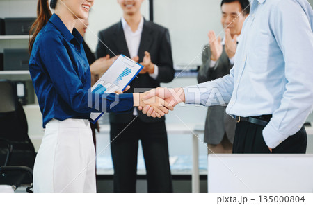 Asian business professionals shaking hands and celebrating success in a modern office, symbolizing teamwork, partnership Asian business professionals shaking hands and celebrating success in a modern office, symbolizing teamwork, partnership 135000804