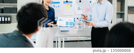 Asian business team presenting charts and reports in modern office meeting, showcasing teamwork, communication, and corporate strategy 135000808