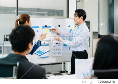 Smiling Asian business team shaking hands after successful meeting, symbolizing partnership, teamwork, and corporate success in a modern office 135000810