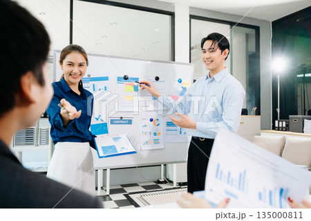 Smiling Asian business team shaking hands after successful meeting, symbolizing partnership, teamwork, and corporate success in a modern office 135000811