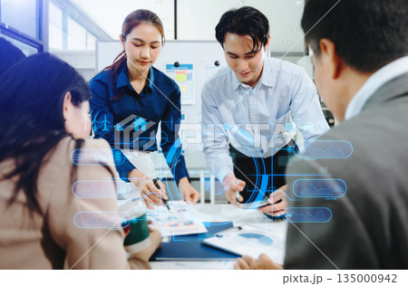 Asian business team brainstorming and discussing reports in bright modern office, showing teamwork, leadership, and creative collaboration 135000942