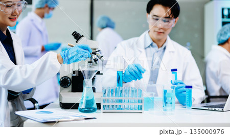 cientists working together in a modern lab with microscopes and blue liquids, symbolizing chemistry, biotechnology, and scientific innovation. 135000976