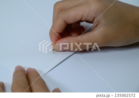 紙に刺さったホッチキスの針を抜く子供の手元 135002572