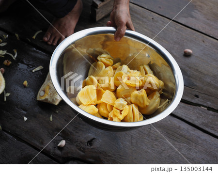 Hand holding metal bowl jackfruit pod, tropical fruit preparation on rustic wooden table, natural organic food vibe 135003144