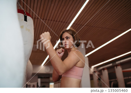 Woman training kickboxing on punching bag in gym. 135005460