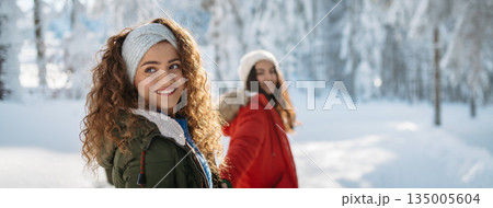 Two female friends walking in winter forest during holidays Two female friends walking in winter forest during holidays 135005604