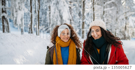 Two female friends walking in winter forest during holidays Two female friends walking in winter forest during holidays 135005627