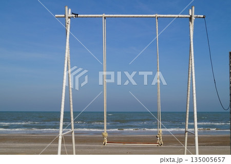 A beautiful place on the stone seashore with a swing against the backdrop of a blue sky and turquoise sea. 135005657