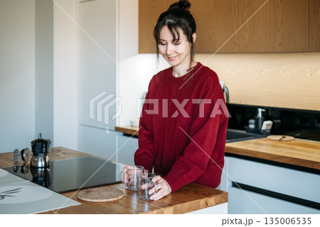 Woman places glass mugs on wooden counter near moka pot in kitchen. Artisanal coffee preparation, home brewing techniques, third-wave coffee culture. Woman places glass mugs on wooden counter near moka pot in kitchen. Artisanal coffee preparation, home brewing techniques, third-wave coffee culture. 135006535
