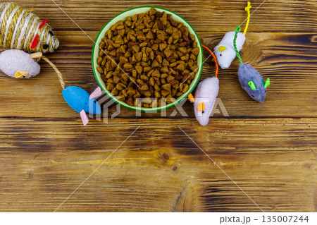 Set of mouses toys for cat and bowl with dry pet food on wooden background. Top view, copy space. Pet care concept Set of mouses toys for cat and bowl with dry pet food on wooden background. Top view, copy space. Pet care concept 135007244