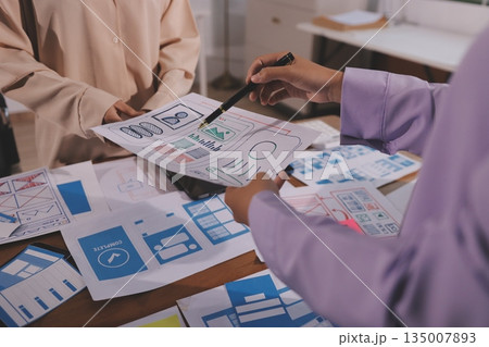 Close up ux developer and ui designer brainstorming about mobile app interface wireframe design on table with customer breif and color code at modern office.Creative digital development agency. 135007893