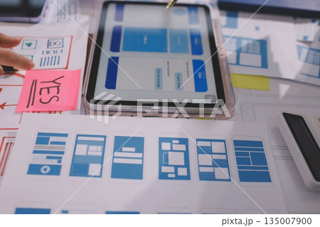 Close up ux developer and ui designer brainstorming about mobile app interface wireframe design on table with customer breif and color code at modern office.Creative digital development agency. Close up ux developer and ui designer brainstorming about mobile app interface wireframe design on table with customer breif and color code at modern office.Creative digital development agency. 135007900