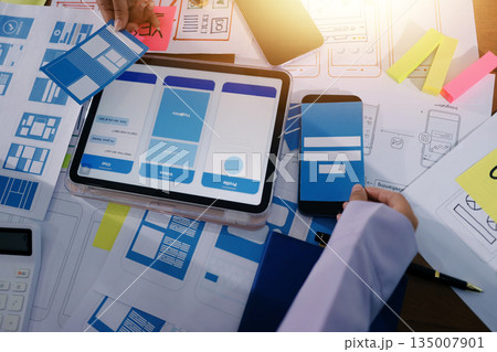 Close up ux developer and ui designer brainstorming about mobile app interface wireframe design on table with customer breif and color code at modern office.Creative digital development agency. 135007901