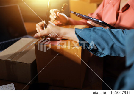 Startup SME small business entrepreneur of freelance Asian woman wearing apron using laptop and box to receive and review orders online to prepare to pack sell to customers, online sme business ideas. Startup SME small business entrepreneur of freelance Asian woman wearing apron using laptop and box to receive and review orders online to prepare to pack sell to customers, online sme business ideas. 135007931