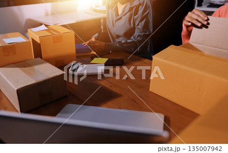 Startup SME small business entrepreneur of freelance Asian woman wearing apron using laptop and box to receive and review orders online to prepare to pack sell to customers, online sme business ideas. 135007942
