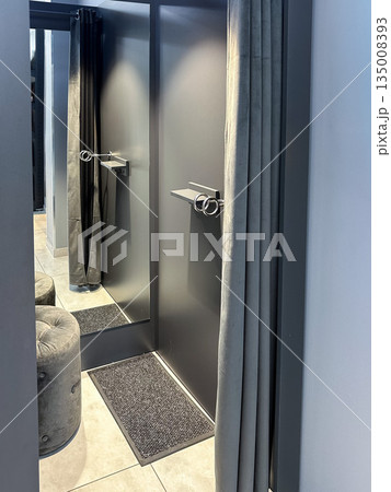 Modern fitting room with mirror, gray curtain, and stool. 135008393