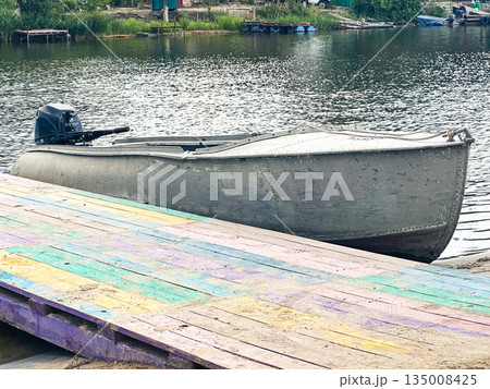 A rustic motorboat on a colorful dock by a calm lake. A rustic motorboat on a colorful dock by a calm lake. 135008425