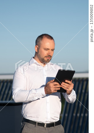 Man in white shirt holding tablet device while thinking outdoors Man in white shirt holding tablet device while thinking outdoors 135009802