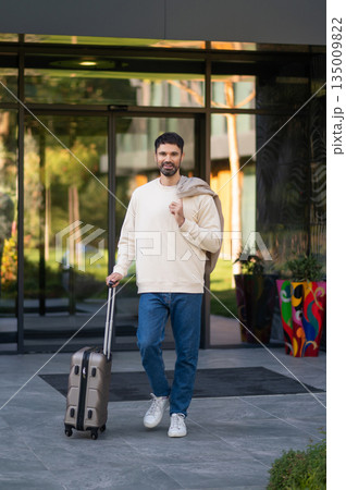 Confident handsome man with a suitcase the hotel entrance Confident handsome man with a suitcase the hotel entrance 135009822